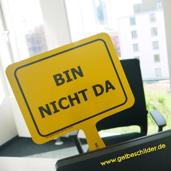 Gelbes Schild mit Textaufschrift „Bin nicht da“ wird in Büro hinter Computer hochgehalten