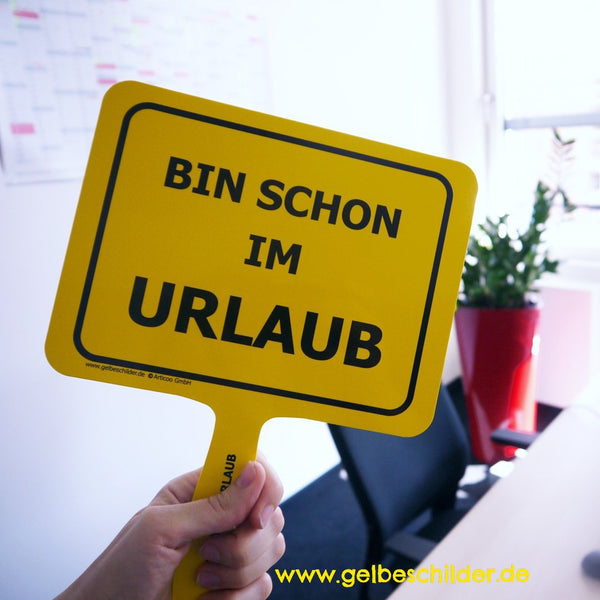 Hand hält in Büro gelbes Schild hoch mit Textaufschrift „Bin schon im Urlaub“