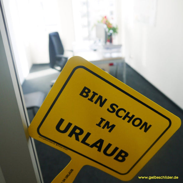 Gelbes Schild mit Textaufschrift „Bin schon im Urlaub“ wird aus Büro gehalten