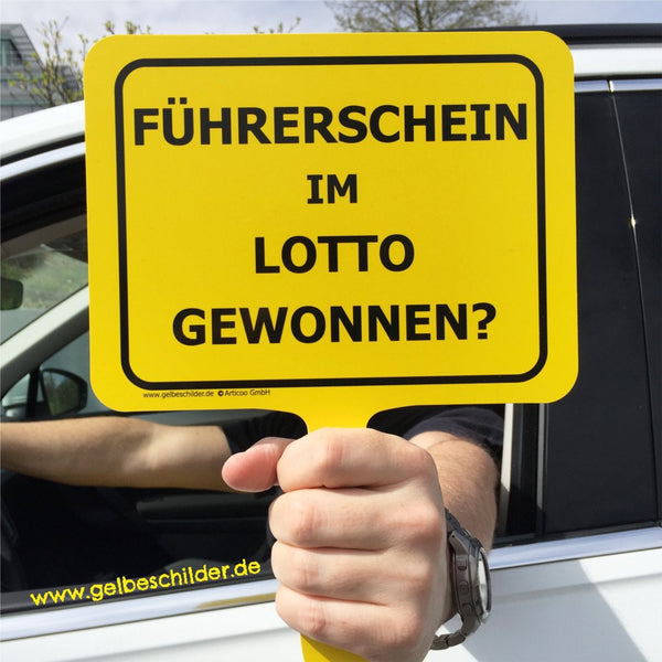 Autofahrer hält gelbes Schild mit Textaufschrift "Führerschein im Lotto gewonnen" aus dem Fenster 