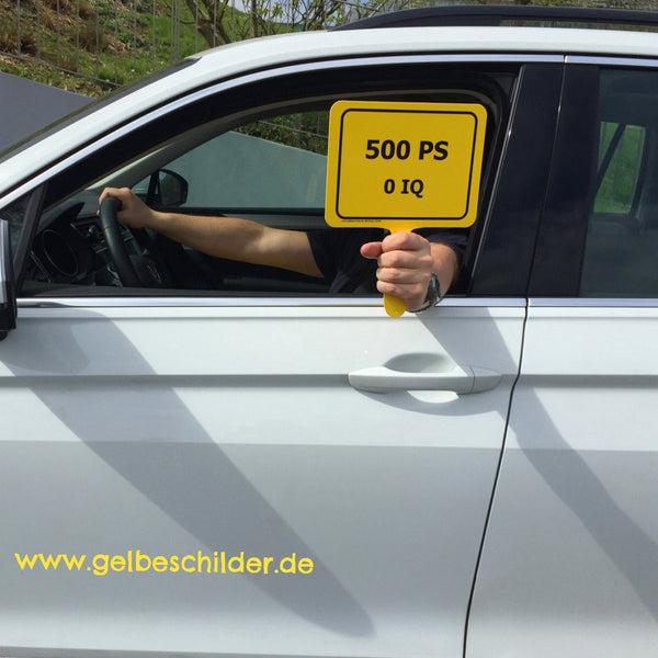 Autofahrer hält gelbes Schild mit Textaufschrift "500 PS - 0 IQ" aus weißem Auto