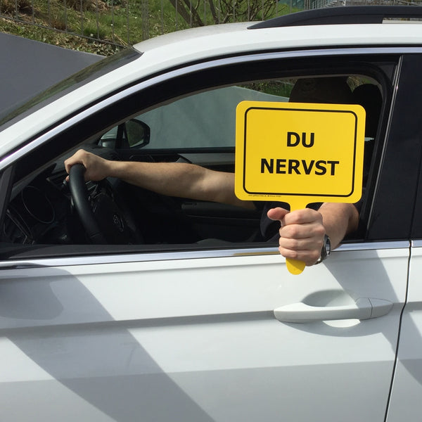 Autofahrer hält gelbes Schild mit Textaufschrift "Du nervst" aus dem Fenster 