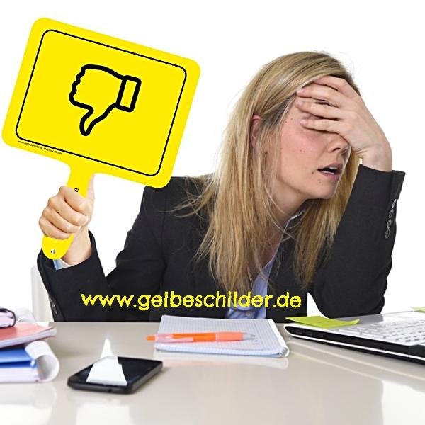 Frau im Büro hält gelbes Schild mit Symbol "Daumen runter" in der Hand